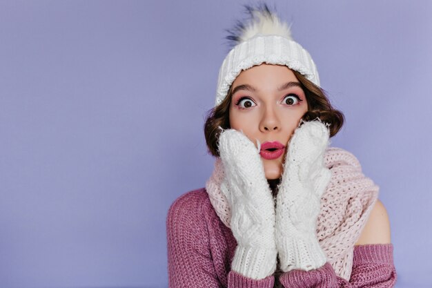 Ritratto di bella donna in guanti bianchi isolati sulla parete viola. adorabile ragazza bruna in cappello che esprime emozioni sorprese.