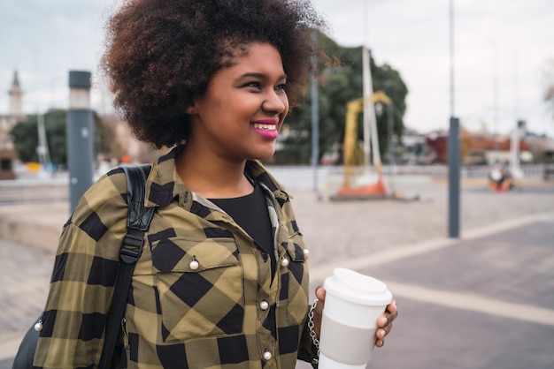 Ritratto di bella donna latina afroamericana che tiene una tazza di caffè all'aperto in strada. Concetto urbano.