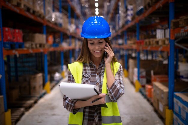 Ritratto di bella donna magazziniere che ha conversazione sul telefono cellulare nel grande centro di distribuzione di stoccaggio