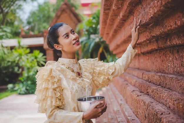 Ritratto di bella donna nel festival di Songkran con il costume tradizionale tailandese nel tempio che tiene una ciotola d'acqua e un sorriso Cultura thailandese con il festival dell'acqua