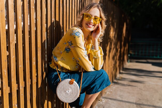 Ritratto di bella donna sorridente alla moda bionda in occhiali da sole da portare della camicetta gialla