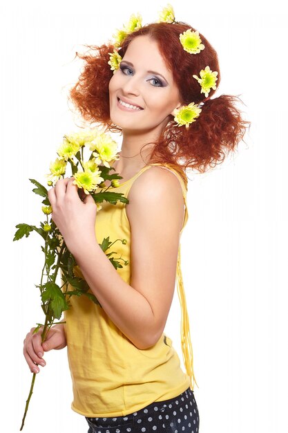 Ritratto di bella donna sorridente dello zenzero di redhead in panno giallo che tiene i fiori e i fiori gialli in capelli isolati su bianco