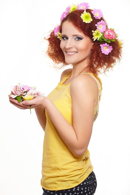 Ritratto di bella donna sorridente dello zenzero di redhead in panno giallo con i fiori variopinti rosa gialli in capelli isolati sui fiori bianchi della tenuta