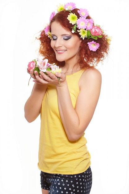 Ritratto di bella donna sorridente dello zenzero di redhead in panno giallo con i fiori variopinti rosa gialli in capelli isolati sui fiori bianchi della tenuta