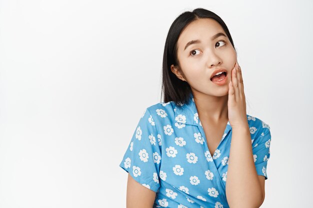 Ritratto di bella giovane donna asiatica che tocca la sua pelle guardando da parte il concetto di cosmetologia della pelle del viso pulita e sana e fondo bianco di trucco