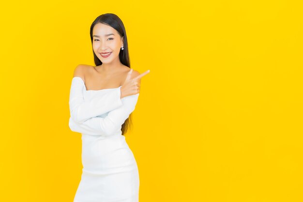 Ritratto di bella giovane donna asiatica di affari che sorride con il vestito bianco sulla parete gialla