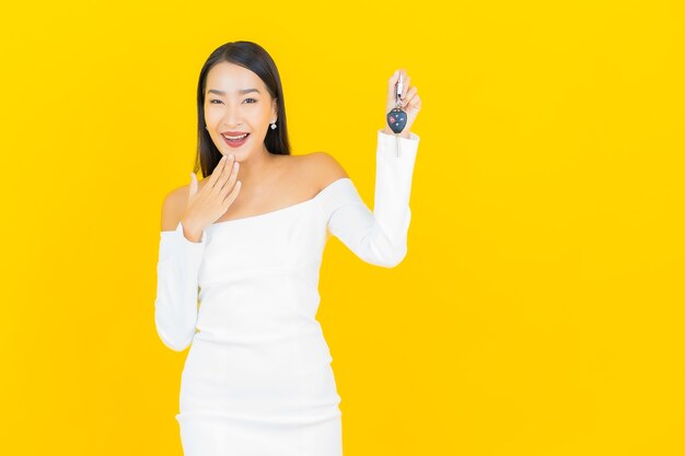 Ritratto di bella giovane donna asiatica di affari con la chiave dell'automobile sulla parete gialla