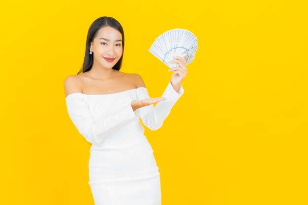 Ritratto di bella giovane donna asiatica di affari con un sacco di soldi in contanti sulla parete gialla