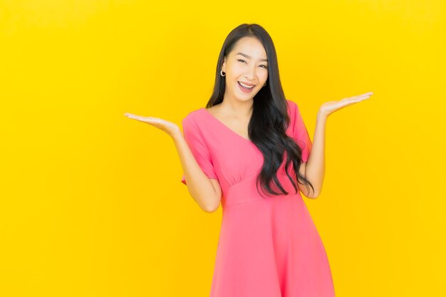 Ritratto di bella giovane donna asiatica sorride in abito rosa sulla parete gialla