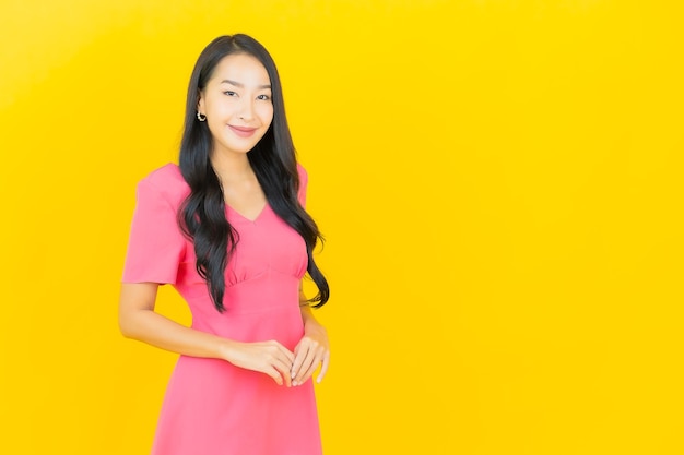 Ritratto di bella giovane donna asiatica sorride in abito rosa sulla parete gialla