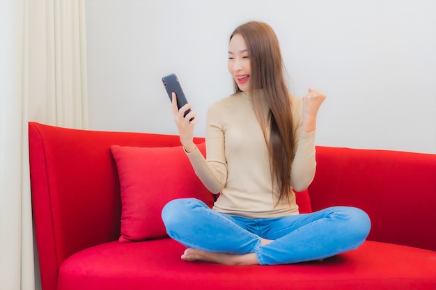 Ritratto di bella giovane donna asiatica utilizza lo smartphone sul divano nell'interno del soggiorno