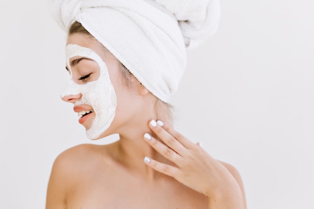 Ritratto di bella giovane donna con asciugamani dopo fare il bagno fa maschera cosmetica sul viso.