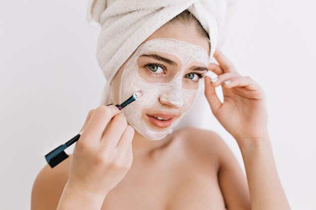 Ritratto di bella giovane donna con asciugamani dopo fare il bagno fa maschera cosmetica sul viso.