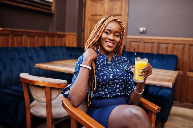 Ritratto di bella giovane donna d'affari africana indossare su camicetta blu e gonna seduta con succo di frutta nella caffetteria
