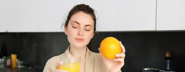 Ritratto di bella giovane donna in buona salute con l'arancia in mano beve il succo appena spremuto