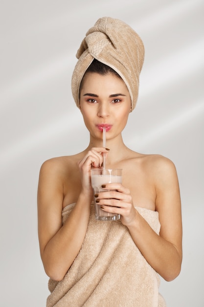 Ritratto di bella giovane donna sciccosa dopo il bagno che sta coperto in asciugamano.