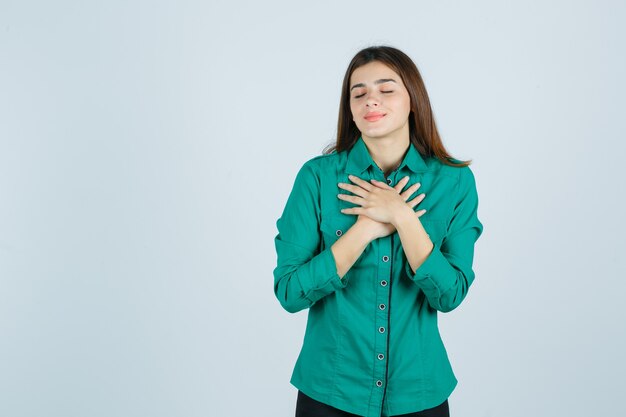 Ritratto di bella giovane signora che tiene le mani sul petto in camicia verde e guardando felice vista frontale