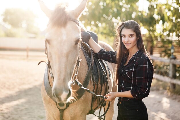 Ritratto di bella proprietaria di fattoria femminile dai capelli lunghi elegante Donna che gestisce un'attività di allevamento di successo che accarezza un cavallo