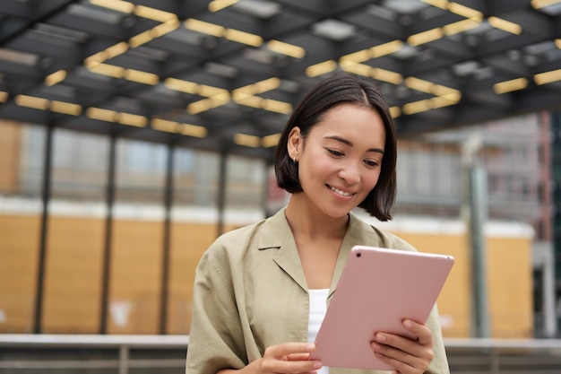 Ritratto di bella ragazza asiatica che usa la lettura del tablet guardando il tablet mentre si è in piedi sulla strada