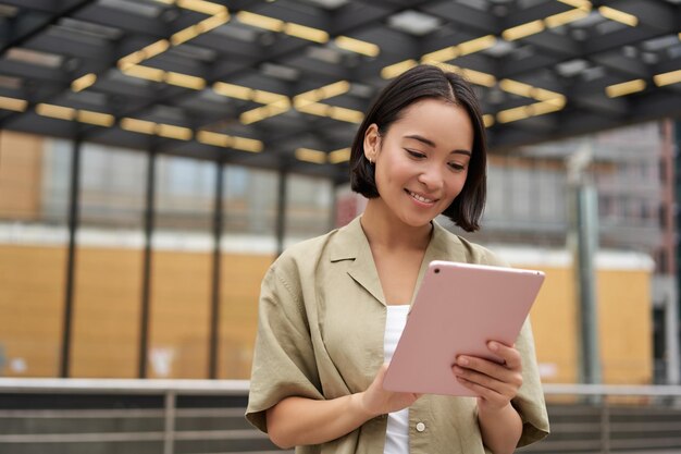 Ritratto di bella ragazza asiatica che usa la lettura del tablet guardando il tablet mentre si è in piedi sulla strada