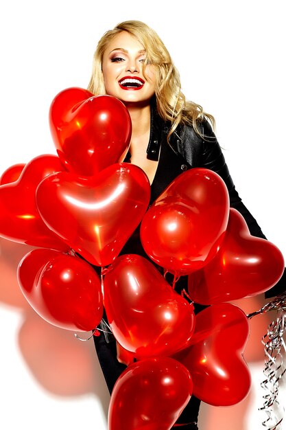 Ritratto di bella ragazza bionda sorridente dolce felice che tiene nelle sue mani palloncini cuore rosso in abiti casual nero hipster