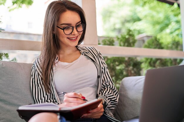 Ritratto di bella ragazza che lavora a casa con laptop e notebook.