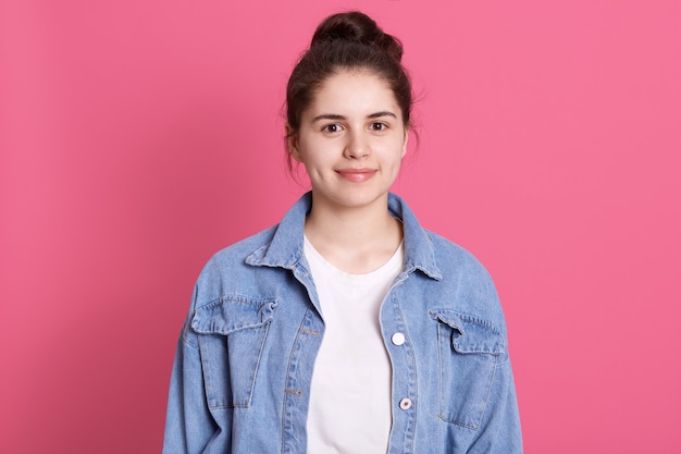 Ritratto di bella ragazza con panino in giacca di jeans e maglietta bianca con un sorriso gentile sul rosa