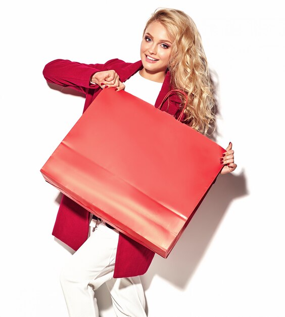 Ritratto di bella ragazza felice felice dolce sorpresa bionda donna con in mano grande borsa della spesa in abiti rossi hipster isolato su bianco