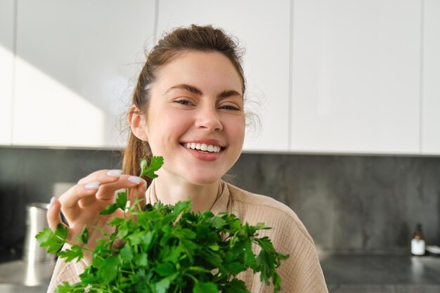 Ritratto di bella ragazza sorridente con il mazzo di prezzemolo in piedi in cucina e cucina
