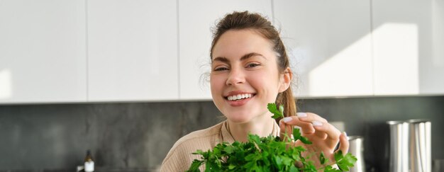 Ritratto di bella ragazza sorridente con il mazzo di prezzemolo in piedi in cucina e cucina