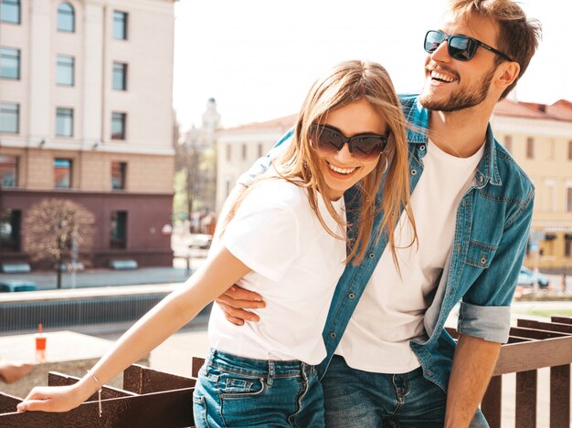 Ritratto di bella ragazza sorridente e il suo bel ragazzo in abiti estivi casual e occhiali da sole. . Abbracciare