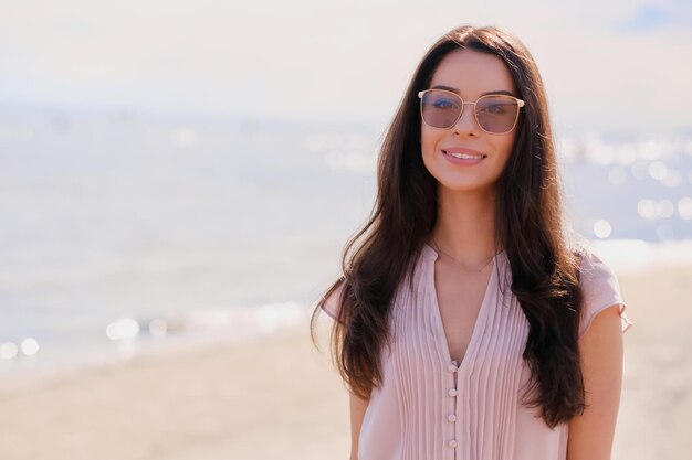 Ritratto di bella ragazza sorridente in occhiali da sole e vestito rosa al mare calmo.