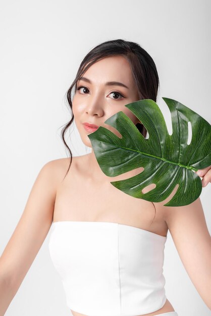 Ritratto di bellezza attraente donne asiatiche in moda in posa con foglia verde organica che indossa un abito bianco su sfondo bianco per cosmetici o salute media