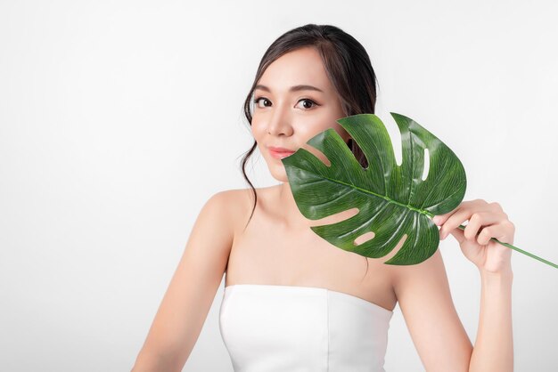 Ritratto di bellezza attraente donne asiatiche in moda in posa con foglia verde organica che indossa un abito bianco su sfondo bianco per cosmetici o salute media