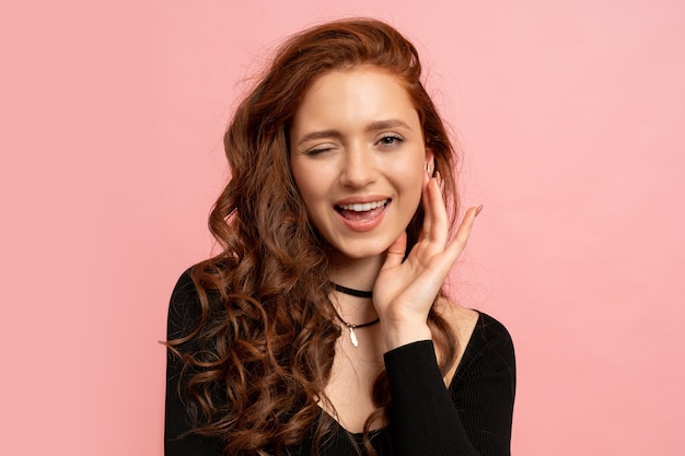 ritratto di bellezza della donna capa rossa che posa sopra la parete rosa. Capelli ondulati. Sorriso perfetto.