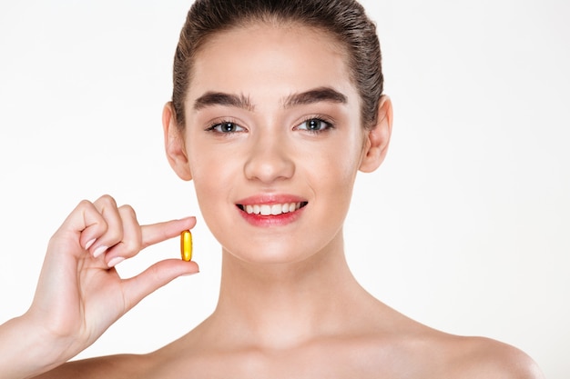 Ritratto di bellezza della donna in buona salute sorridente con i meds o la vitamina della capsula della tenuta dei capelli scuri nella sua posa della mano