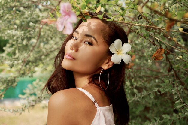 Ritratto di bellezza della ragazza asiatica felice con bel viso esotico in posa in giardino.