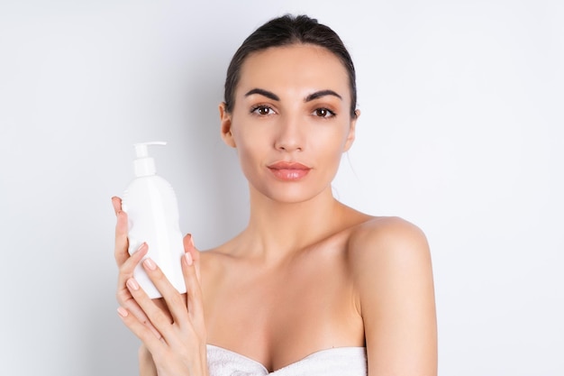 Ritratto di bellezza vicino di una donna in topless con pelle perfetta e trucco naturale che tiene una bottiglia di lozione per il corpo shampoo su uno sfondo biancox9