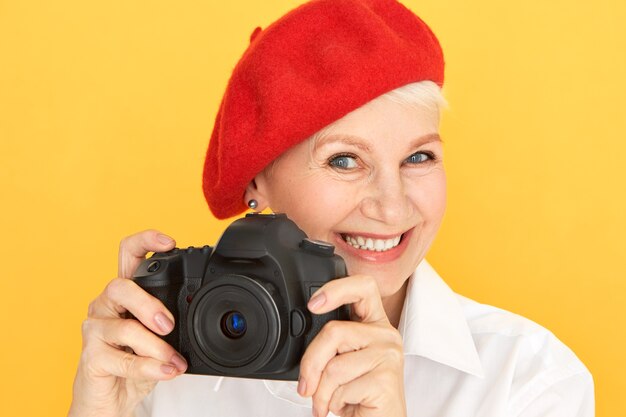 Ritratto di bello fotografo femminile maturo energico con capelli corti e rughe che prendono le immagini usando la macchina fotografica professionale nera