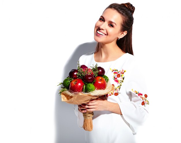 Ritratto di bello modello caucasico sorridente della donna del brunette in vestito alla moda da estate bianca con il mazzo creativo insolito dei fiori