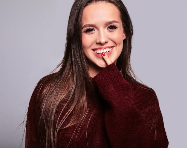 Ritratto di bello modello felice felice della donna del brunette in vestiti casuali del maglione rosso caldo isolati su gray con trucco di sera e le labbra variopinte