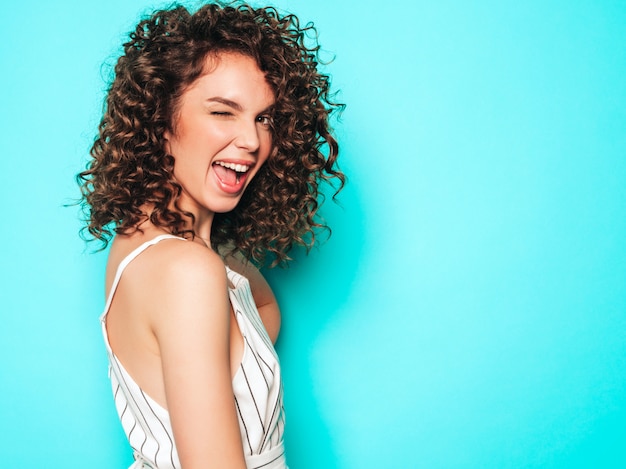 Ritratto di bello modello sorridente con l'acconciatura dei riccioli di afro vestita in vestiti dei pantaloni a vita bassa di estate Ragazza spensierata sexy che posa vicino alla parete blu Donna divertente e positiva alla moda