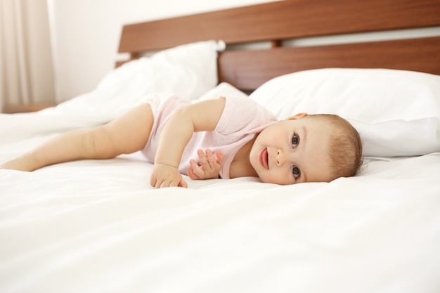 Ritratto di bello neonato sveglio che mostra lingua che si trova sul letto a casa.