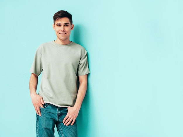 Ritratto di bello sorridente elegante hipster modello lambersexual Uomo vestito con maglietta e jeans Moda maschio isolato in studio in posa vicino al muro blu Allegro e felice