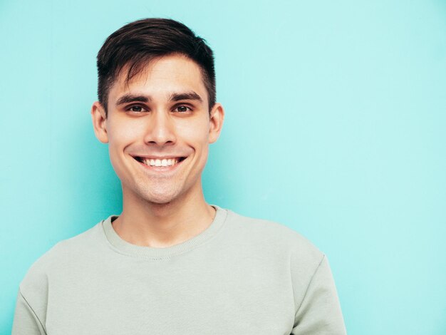 Ritratto di bello sorridente elegante hipster modello lambersexual Uomo vestito con maglietta e jeans Moda maschio isolato in studio in posa vicino al muro blu Allegro e felice