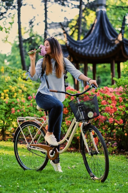 Ritratto di bruna con bicicletta da città vicino al padiglione cinese tradizionale in un parco.