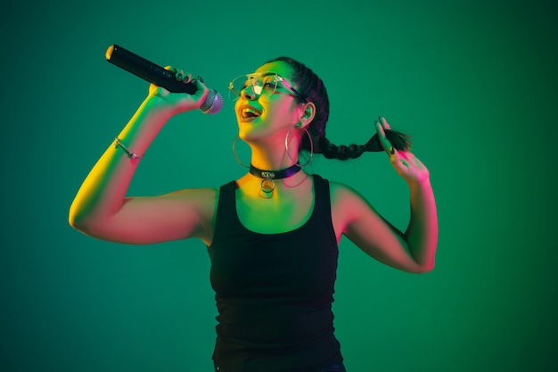 Ritratto di cantante femminile isolato sulla parete verde dello studio in luce al neon