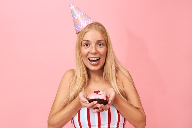 Ritratto di carino affascinante giovane donna con lentiggini, lunghi capelli lisci e bretelle congratulandosi con te per il compleanno