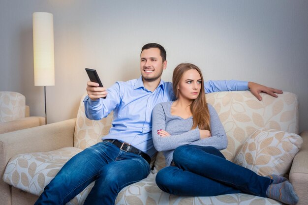 Ritratto di coppia seduta sul divano a guardare la televisione. Immagine di uomo felice con telecomando in mano e donna sconvolta