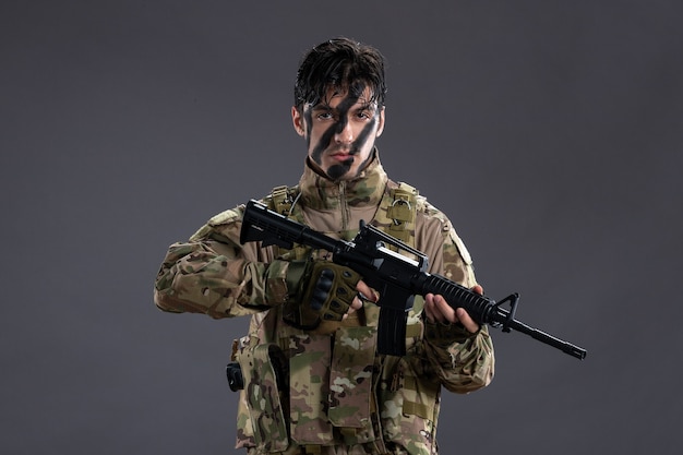 Ritratto di coraggioso soldato in uniforme militare con mitragliatrice sul muro scuro